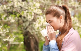 woman blowing her nose outside in front of trees in need of allergy testing