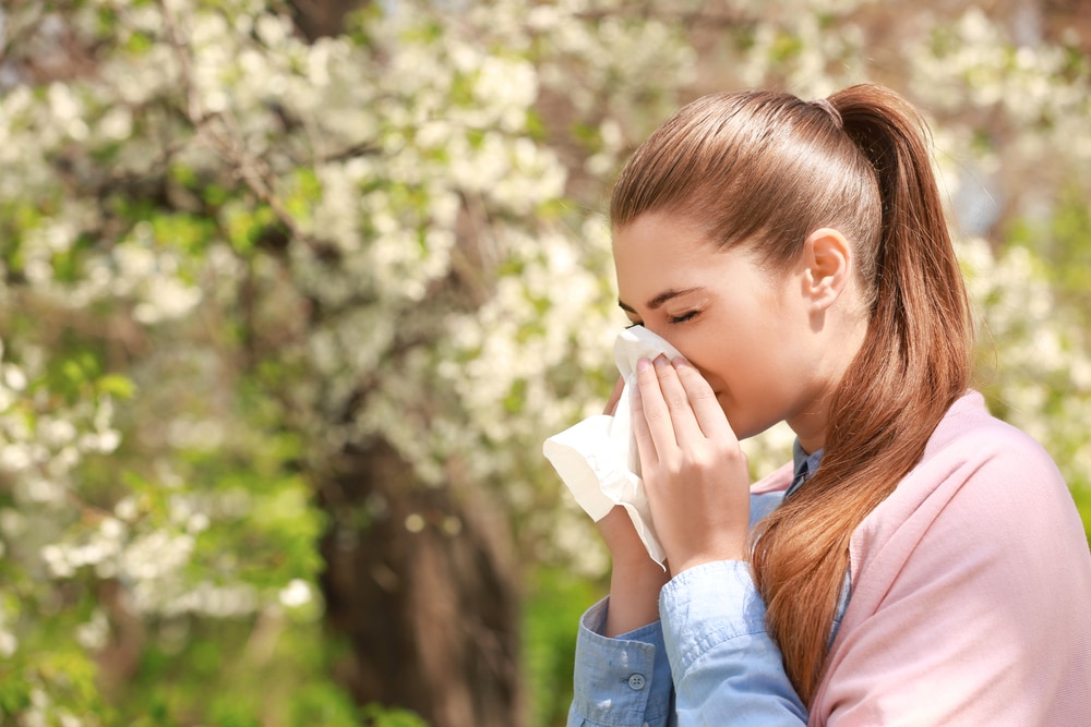 woman blowing her nose outside in front of trees in need of allergy testing